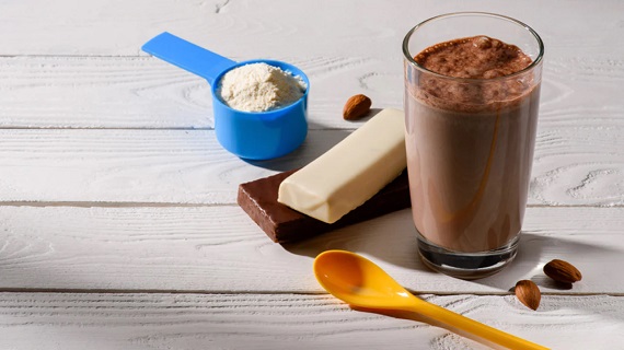 scoop of protein powder an orange plastic spoon and two protein bars placed on top of a wooden table