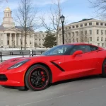 A sleek red sports car parked in front of a historical building with a golden dome.